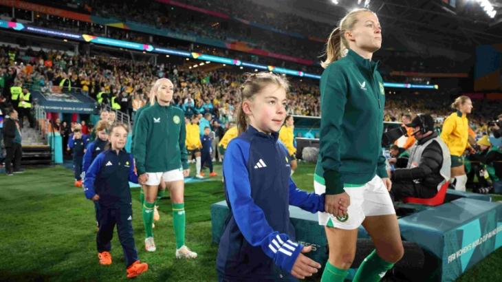 2 Matildas players walking onto a field holding hands of 2 young girls