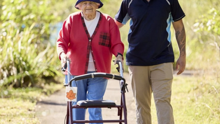 Elderly women walking with help from a carer