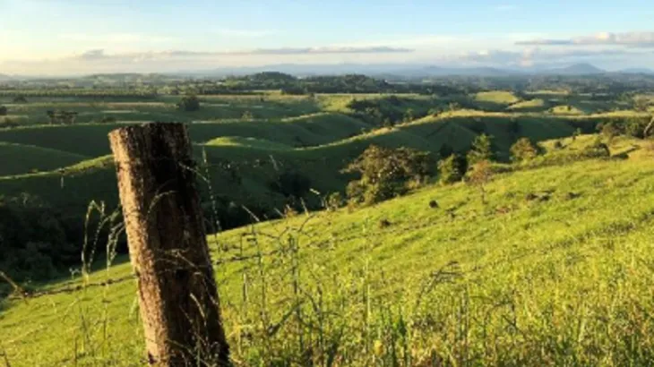 Landscape image of rolling green hills and an old wooden fence post in the foreground