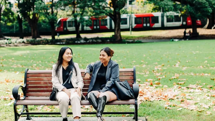 two_young_ethic_women_sitting_and_talking_on_a_park_bench