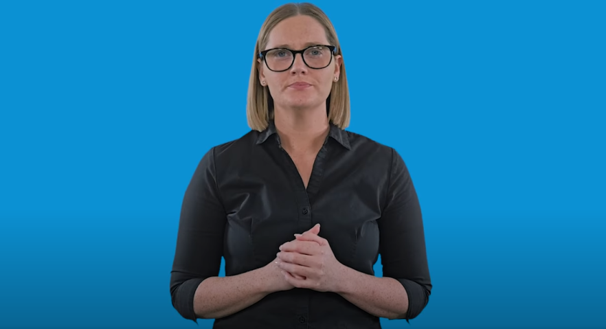 A female Auslan interpreter standing in front of a blue background. 