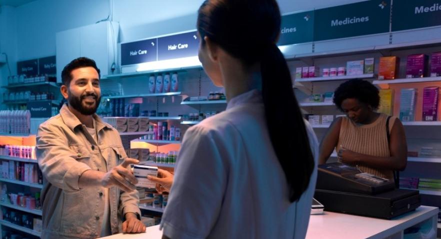 A male Danny picking up medicine from a pharmacy at the counter with a staff member with long hair