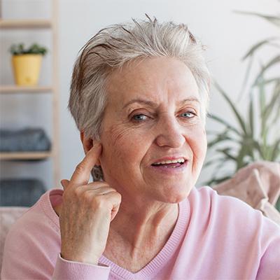 Elderly woman with short hair pointing at her ear